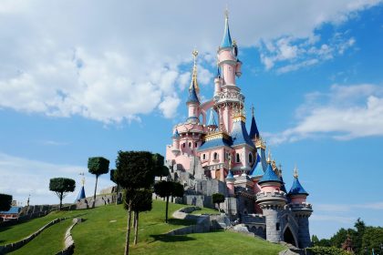 Ein Schloss in rosa und blau auf einem begrünten Hügel