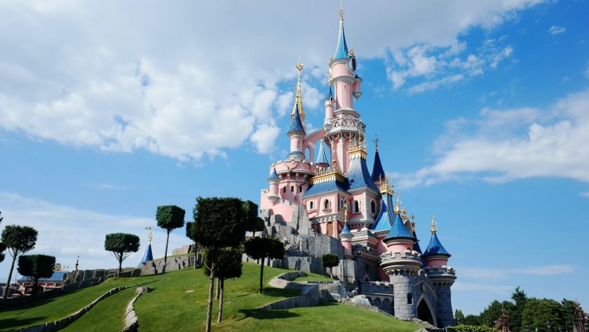 Ein Schloss in rosa und blau auf einem begrünten Hügel